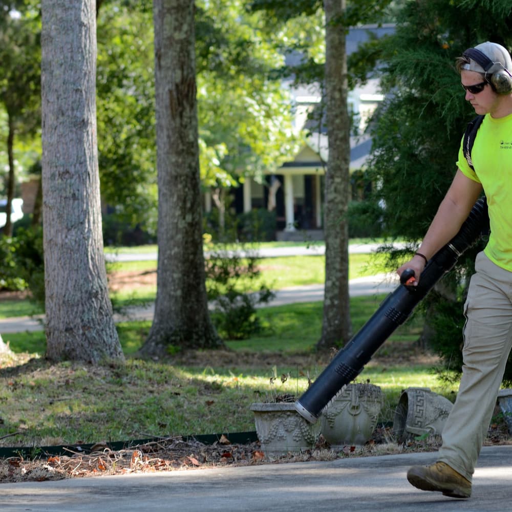 A landscaper working with a leaf blower on a residential property