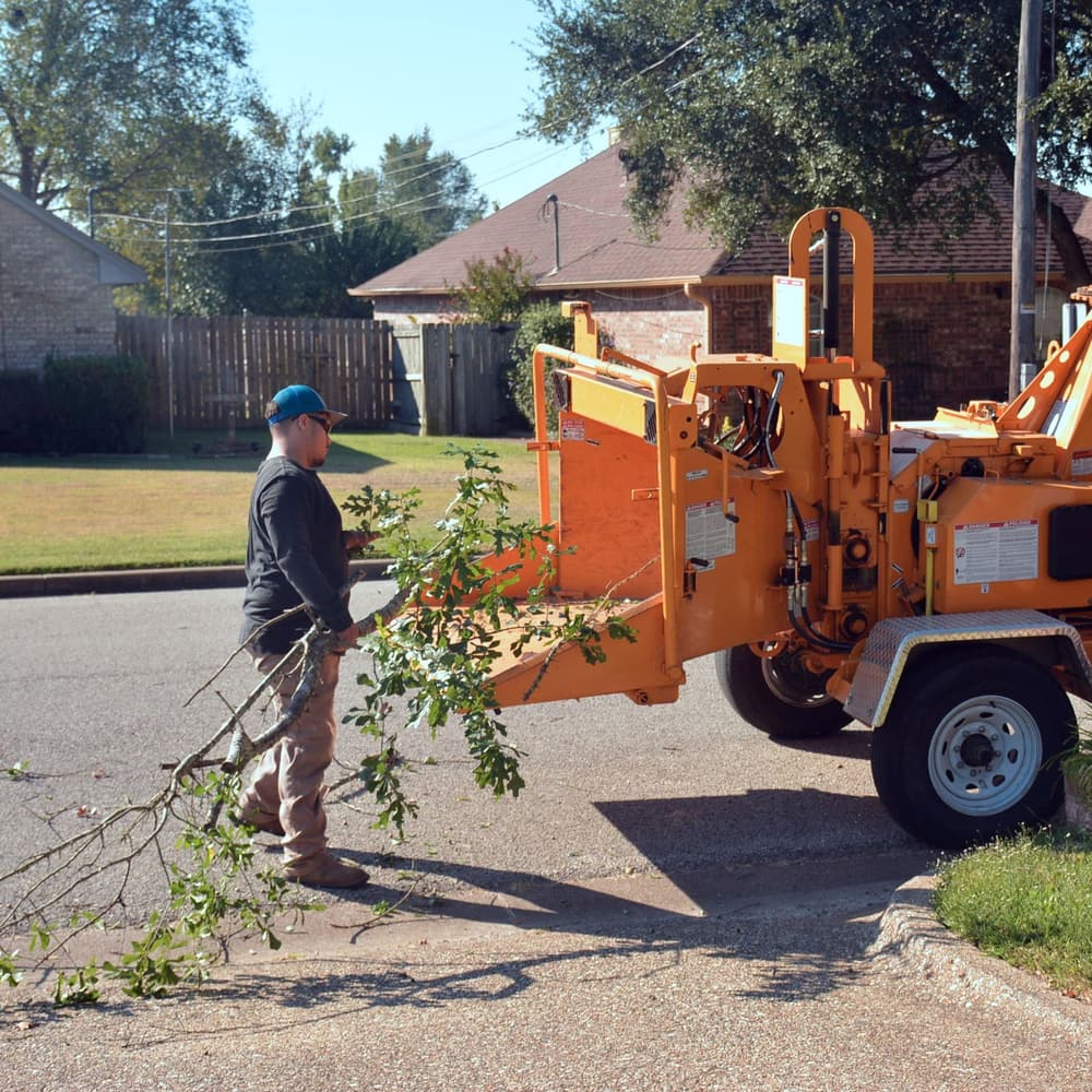 A worker feeding brush into a wood chipper on a residential street