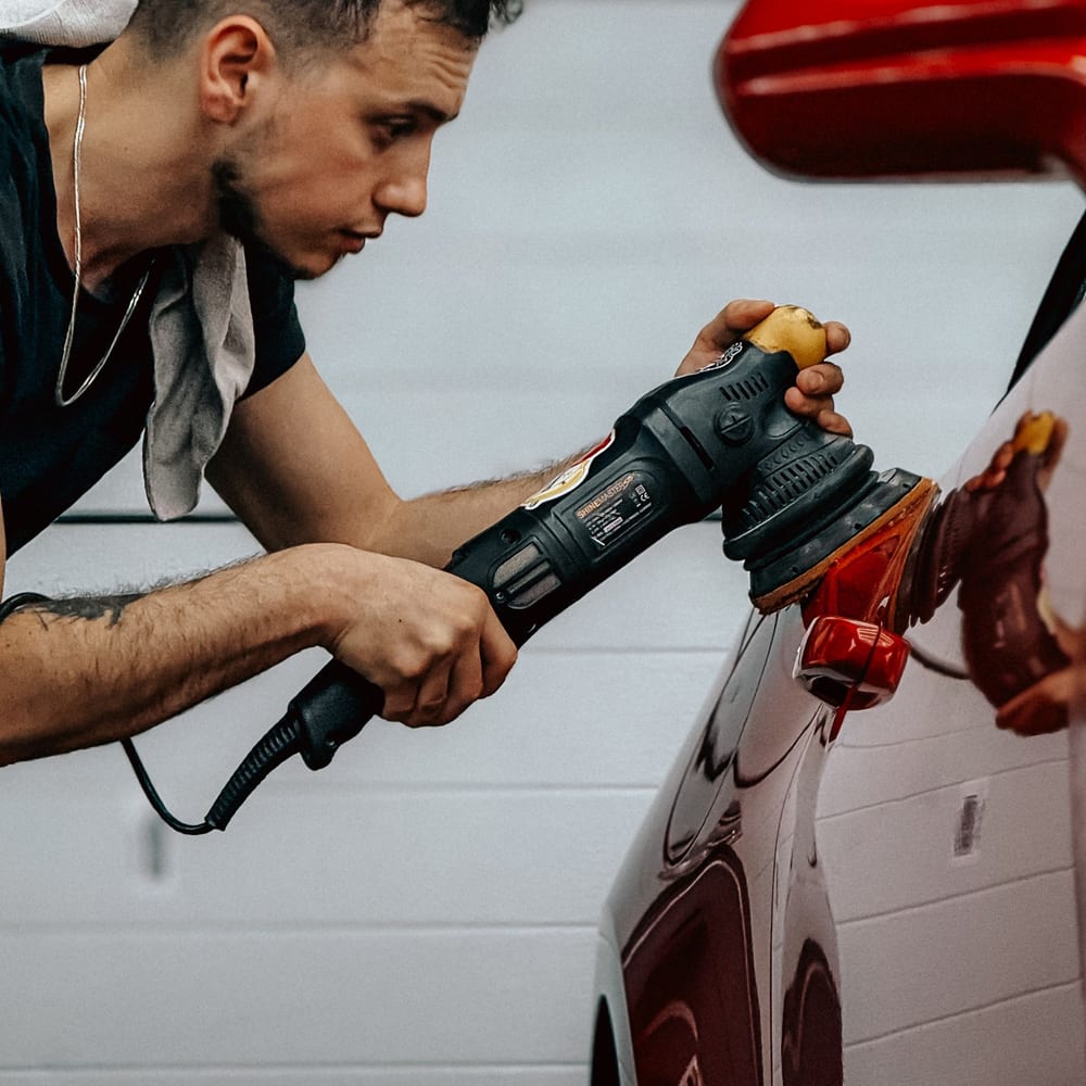 A detailer polishing the panel of a car with a rotary buffer