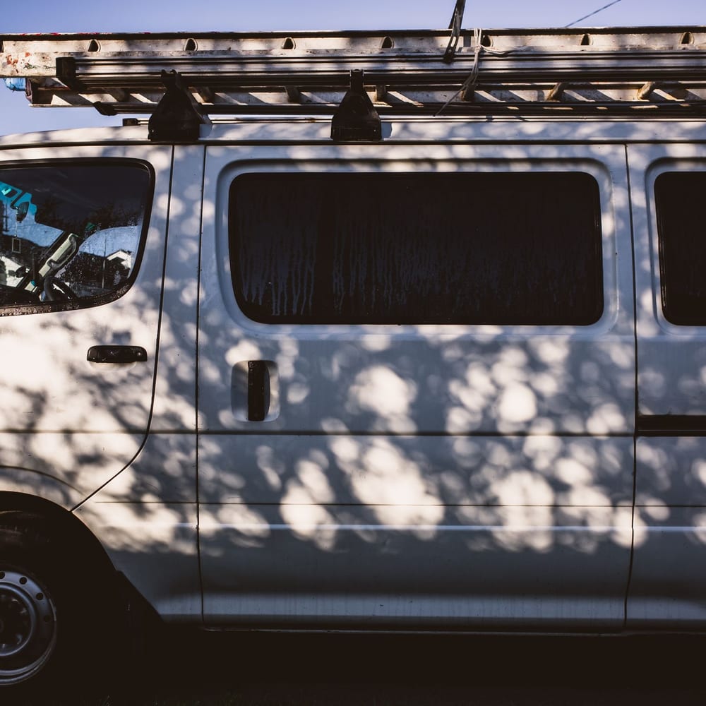A white work van carrying a ladder on its roof rack